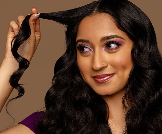 Woman with long wavy black hair holding a strand, showcasing healthy, defined waves with Design Essentials haircare results.