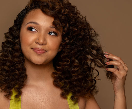 Smiling woman with voluminous defined curly hair wearing a yellow top, showcasing healthy curls styled with Design Essentials products.