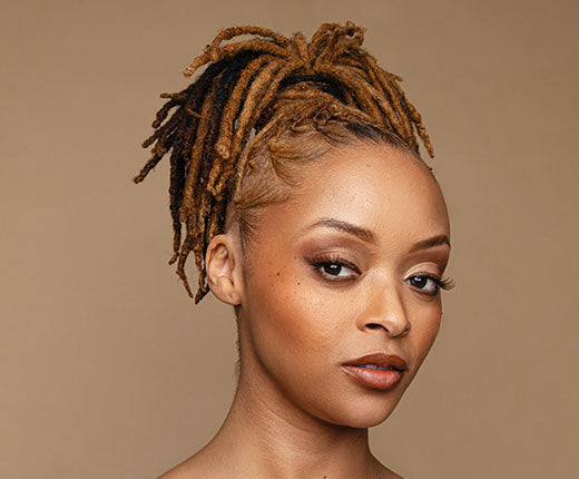 Woman with blonde-tinted locs styled in a high ponytail, showing neat edges and textured loc hairstyle with Design Essentials haircare.