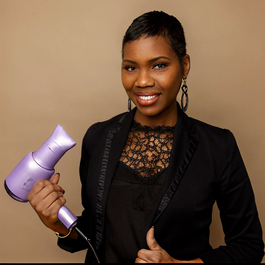 Smiling professional hairstylist holding a purple hairdryer while wearing a black outfit