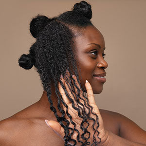 Black woman with natural hair styled in sections demonstrating defined curls and coils after applying Design Essentials hair care products.