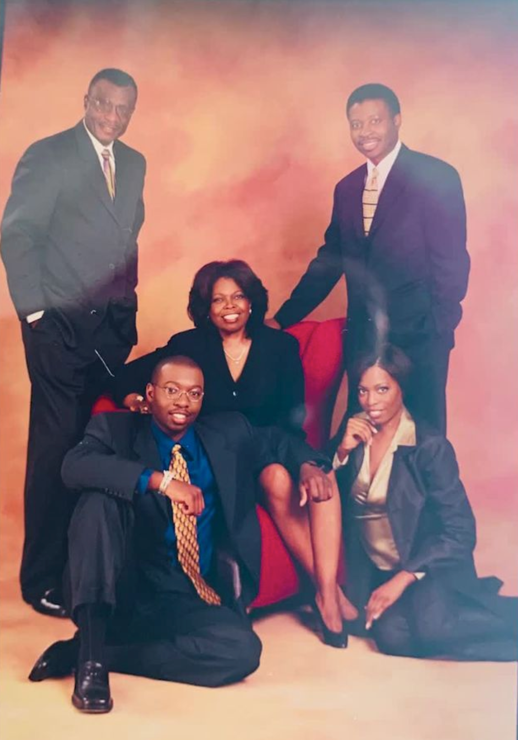 Formal studio portrait of a multi-generation family dressed in suits and historic attire against a painted backdrop.